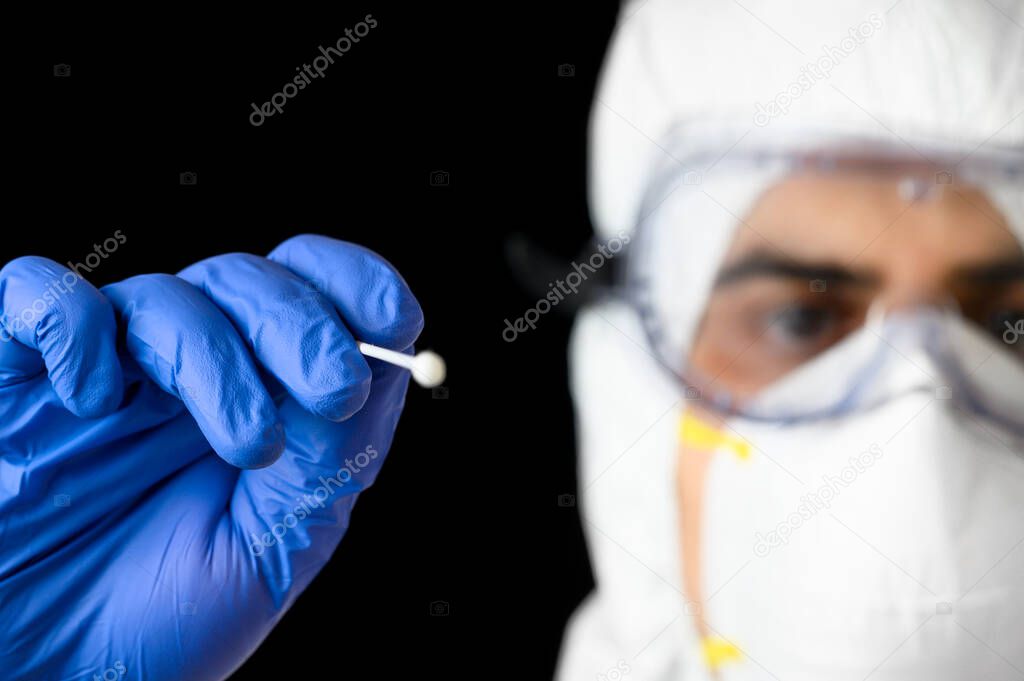Medical healthcare technologist holding COVID-19 swab collection kit, wearing white PPE protective suit mask gloves, test tube for taking patient specimen sample.