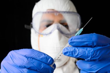 Laboratuvar üniformalı doktor ya da bilim adamı ilaç şişesi ve şırıngayı siyah izole edilmiş arka planda tutuyor..