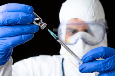 Laboratuvar üniformalı doktor ya da bilim adamı ilaç şişesi ve şırıngayı siyah izole edilmiş arka planda tutuyor..