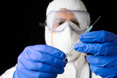 Laboratuvar üniformalı doktor ya da bilim adamı ilaç şişesi ve şırıngayı siyah izole edilmiş arka planda tutuyor..
