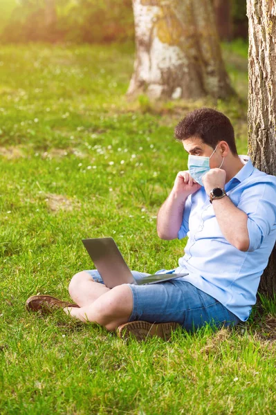Man in protective mask is working with laptop outdoor, during Coronavirus pandemic outrbreak. — Stock Photo, Image