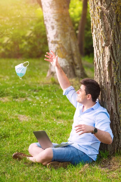 Young man sitting in the park throwing away protective face mask celebrating victory over coronavirus outside in open air. End of quarantine. Remove mask. Outdoor. Freedom. Pandemic crisis end. — Stock Photo, Image