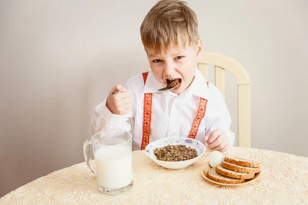 five-year-old in a white shirt child eats lentils