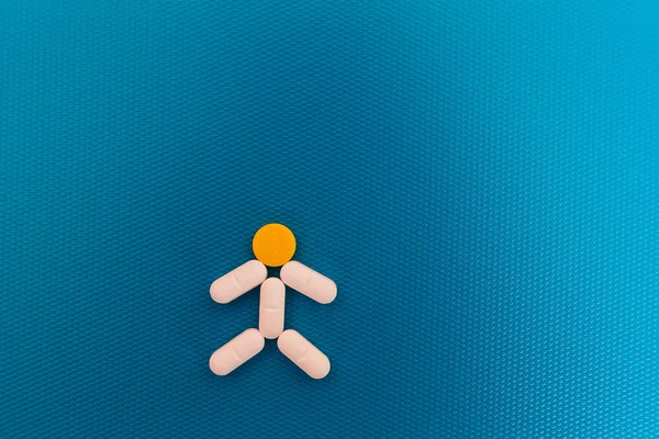 Tabletas en forma de hombre. píldoras blancas y amarillas sobre un fondo azul — Foto de Stock