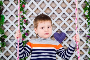 bir kuşak üzerinde bir üç-yıl-yaşlı çocuk portresi. çizgili kazaklı oğlan salıncağa oturur. Bahar ruh hali, çiçek dekorasyon. Tür akıllı çocuk bakmak