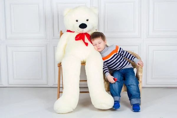 Um abraço de bebé com um urso de peluche enorme. Rapaz sentado na cadeira, olhos fechados. Fundo branco — Fotografia de Stock