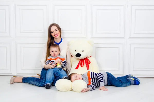 Madre joven con dos hijos y oso de peluche. felicidad familiar, mamá y dos hijos en jeans sentados en el suelo — Foto de Stock