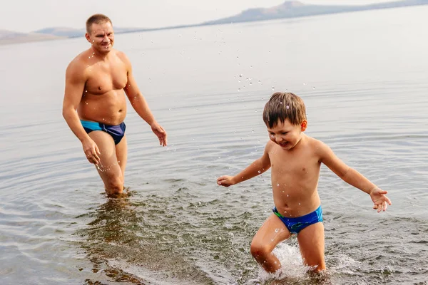 Πατέρας και παιδί παίζουν στη λίμνη. ο άνθρωπος με το παιδί που παίζει στο νερό στην παραλία, συναισθηματική φωτογραφίες — Φωτογραφία Αρχείου