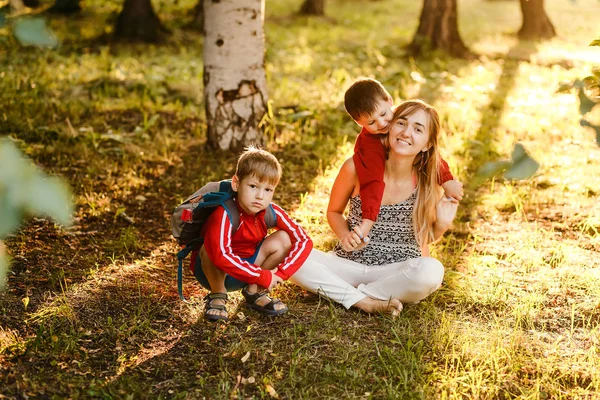 Madre joven con dos hijos sentados en el césped soleado. Familia feliz en las vacaciones de verano en el Parque — Foto de Stock
