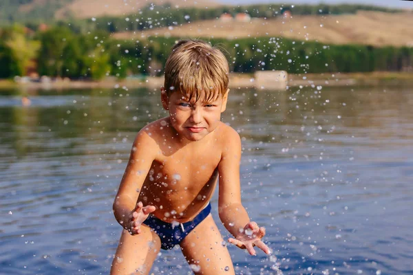 Мальчик плеснул водой в озеро. Плавание в теплом озере в солнечный летний день — стоковое фото