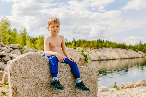 Блондин, сидящий на большом камне на скалистом берегу озера — стоковое фото