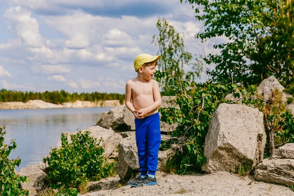 Boy in a cap stands on rocky shore on Sunny summer day — Stock Photo, Image