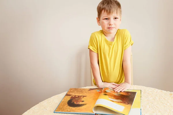 Chlapec v žluté tričko stojí s velkou otevřenou knihu, na bílém pozadí — Stock fotografie