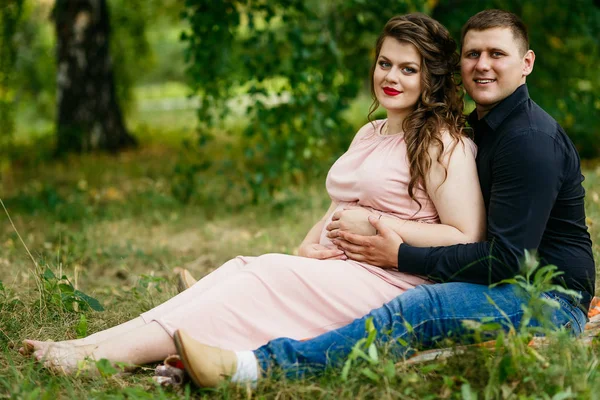 Genç hamile kadın ve kocası çimenlerin üzerinde yeşil park kucaklamak — Stok fotoğraf