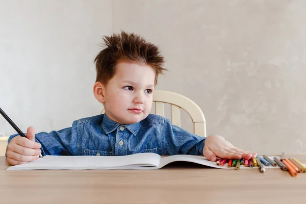 Маленький мальчик с цветным карандашом, сидящий за письменным столом и отводящий взгляд — стоковое фото