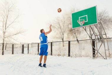 basketbolcu mavi üniformalı kışın bir sokak basketbol sahası üzerinde sepet içine bir basketbol topu atma