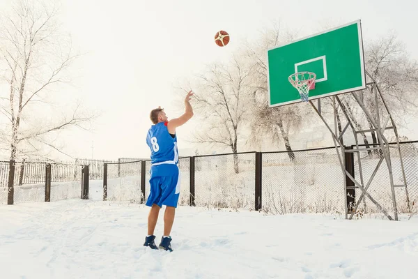 basketbolcu mavi üniformalı kışın bir sokak basketbol sahası üzerinde sepet içine bir basketbol topu atma