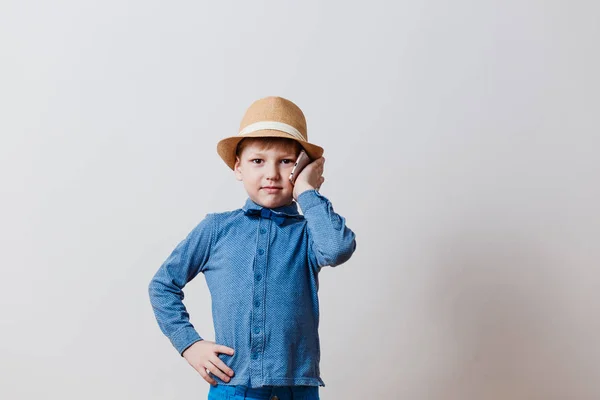 Liten pojke i blå skjorta i hatt som talar i telefon på vit bakgrund — Stockfoto