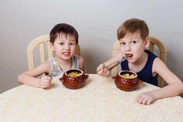 Два маленьких мальчика сидят за столом и едят жареную курицу и картошку — стоковое фото