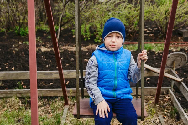 El niño sentado en el columpio de hierro en el jardín en la primavera —  Fotos de Stock