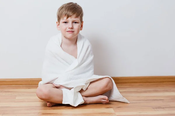 Симпатичный шестилетний мальчик сидит на полу на белом фоне — стоковое фото