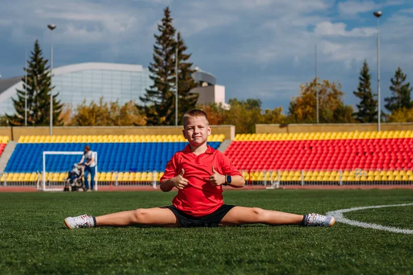 Boy in red T-shirt sits on twine at a sports stadium