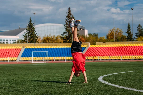 Bir çocuk spor stadyumunda kollarında duruyor.
