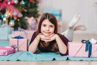 Mutlu kız, siyah saçlı, karnı üstünde, bir Noel ağacının altında yatıyor.