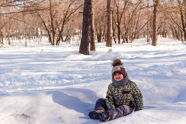 Joyeux garçon souriant assis sur la neige blanche — Photo