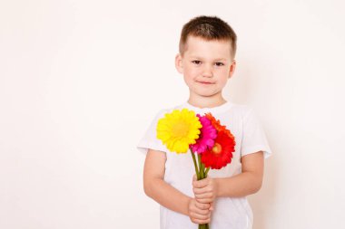 Elinde bir buket gerberayla beyaz tişörtlü yedi yaşında bir çocuk.