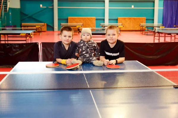 three children playing table tennis near the tennis table indoors