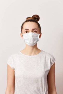 Tıbbi maskeli beyaz bir kadın beyaz arka plandaki kameraya bakıyor. Koronavirüsü durdurun.