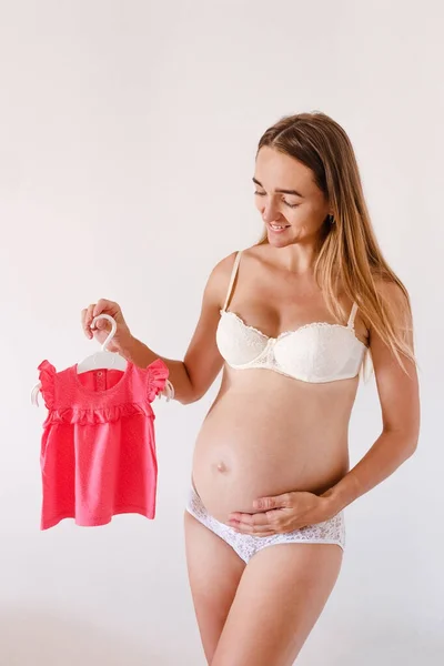 Mujer Embarazada Sostiene Vestido Bebé Cerca Del Vientre Sobre Fondo —  Fotos de Stock