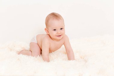 Avrupalı şirin bebek evde tüylü bir battaniyenin üzerinde sürünüyor. Bezli bir bebek. Bir yaşın altındaki çocuklar