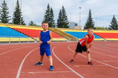 İki beyaz çocuk stadyumdaki bir spor yarışının başlangıcına hazırlanıyor. yüz metre..