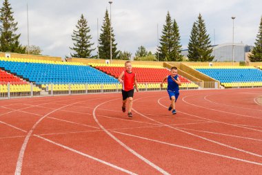 Çocuklar spor stadyumunda koşuyor. Spor üniformalı iki atletik çocuk.