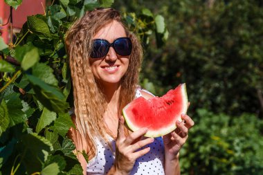 Güneş kremi sürmüş gülümseyen kadın elinde bir dilim kırmızı karpuz tutuyor.