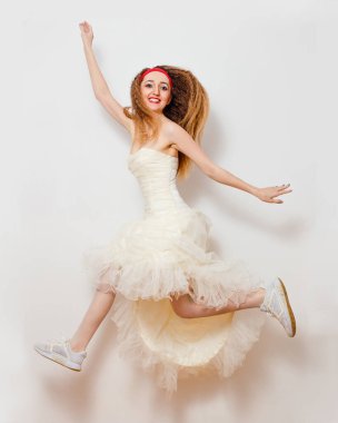 Gelinlik ve spor ayakkabılarla gülümseyen gelin beyaz arka planda zıplıyor.