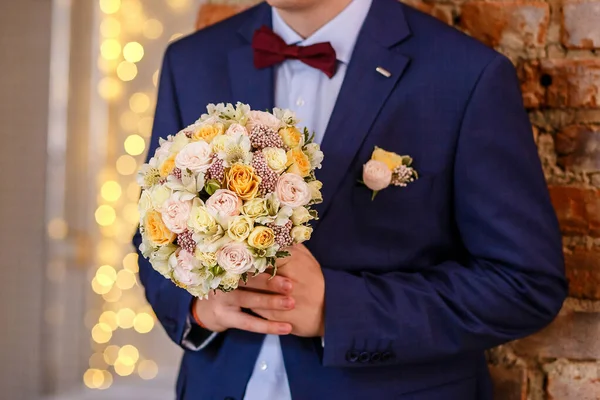 the groom in a jacket with a bud and a bow tie holds a bouquet for the bride. photo of the groom without a face
