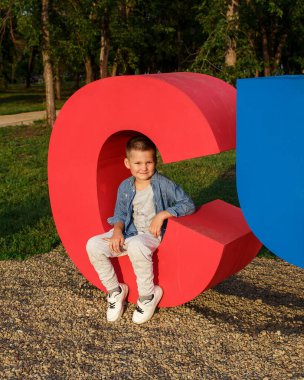 Şirin, gülümseyen bir çocuk açık havada büyük bir plastik mektubun üzerinde oturuyor.