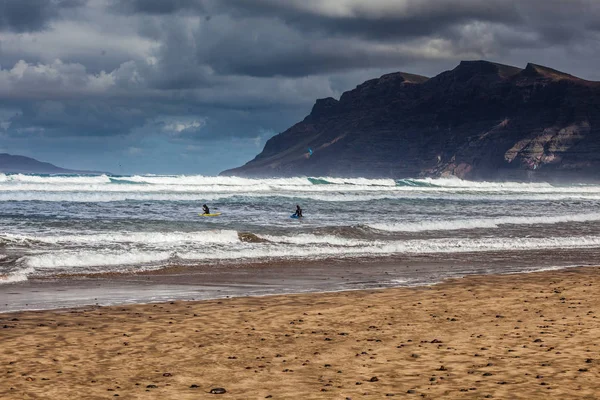 Surfers and kiters into the sea on the surfing beach Famara on Lanzarote — Stok Foto
