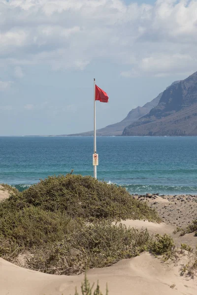 Rudá vlajka váží ve větru na pláži Famara surfaři na Lanza — Stock fotografie