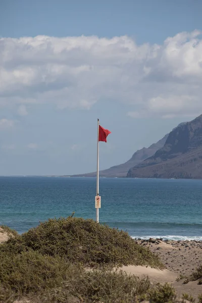 La bandera roja pesa en el viento en Surfers Beach Famara en Lanza —  Fotos de Stock