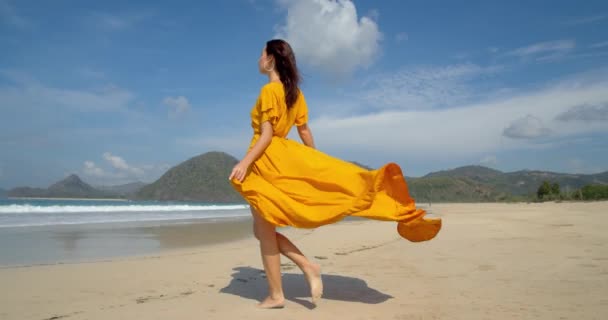 Beautiful barefoot young lady walking on the sunny beach yellow dress fluttering in the wind a great day for a walk
