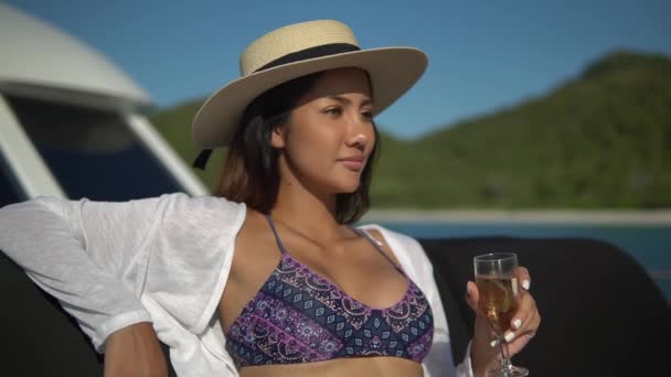 awesome young brunette in white shirt and staw hat sitting on couch on excellent yacht slow motion drinking champagne and sunbathing
