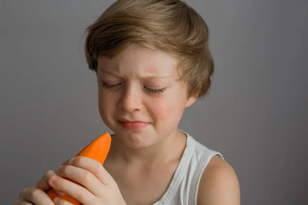 The boy looks at the carrot and frowns — Stock Photo, Image