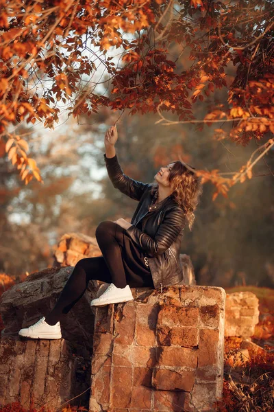 Girl among autumn leaves sitting on the parapet — Stock Photo, Image