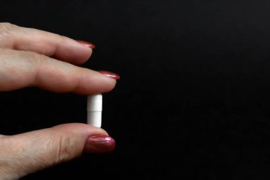 Siyah arka planda iki parmak arasında tıbbi kapsül