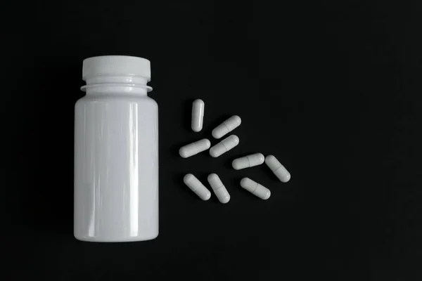 Cápsulas medicação com um frasco aberto no fundo — Fotografia de Stock