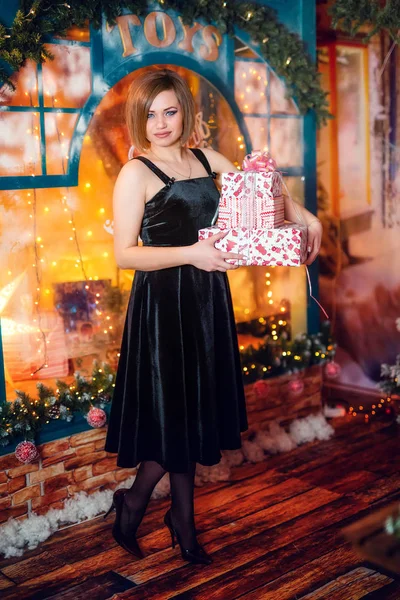 Das Mädchen steht mit Geschenken am Weihnachtsfenster — Stockfoto